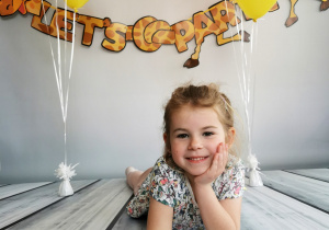 Dziewczynka leży na tle fotograficznym i pozuje do zdjęcia wśród balonów.